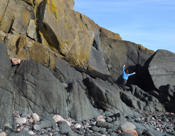 A distance image of a solo dancers on the beach near a rocky cliff