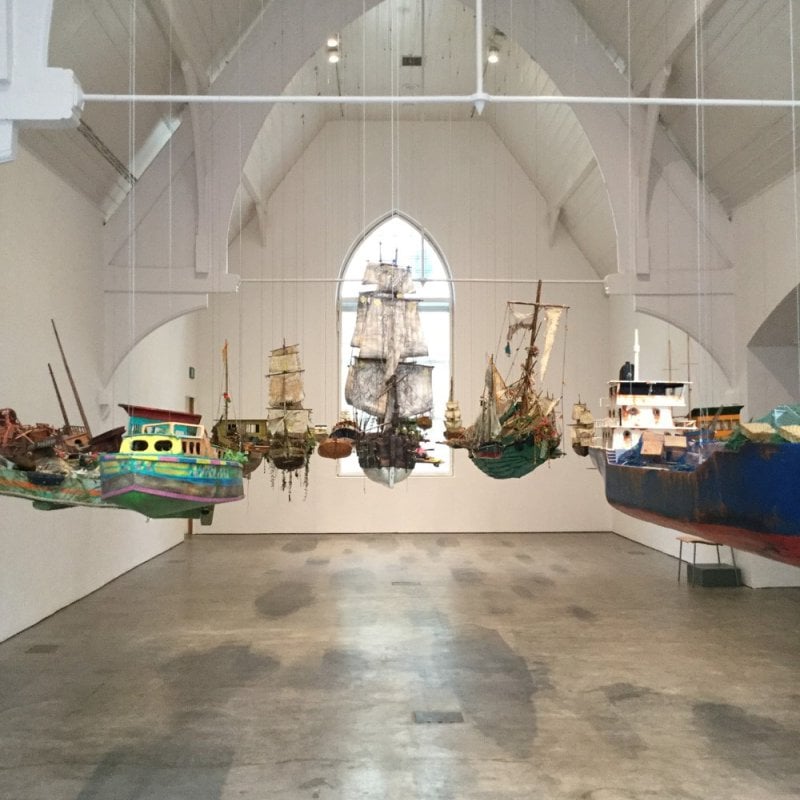 An art installation of some boat sculptures hanging in a gallery