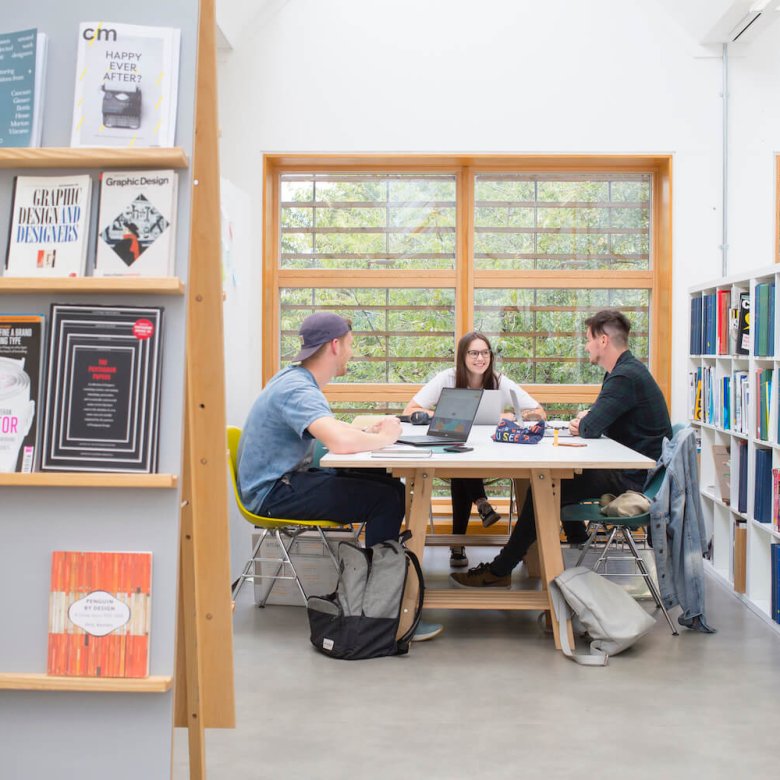 Three students sat at a table in a Graphic Design studio at Falmouth University