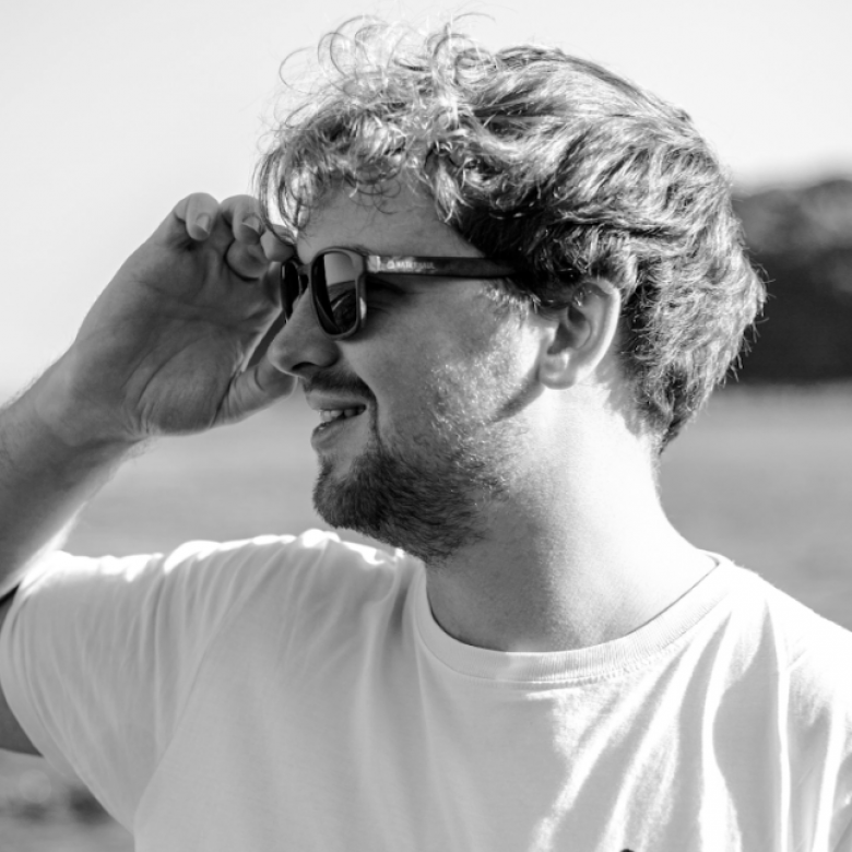 A man looks to his left, wearing sunglasses. The picture is in black and white