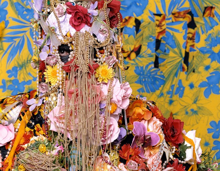 Figure covered in flowers and gold chains with just eyes showing through.
