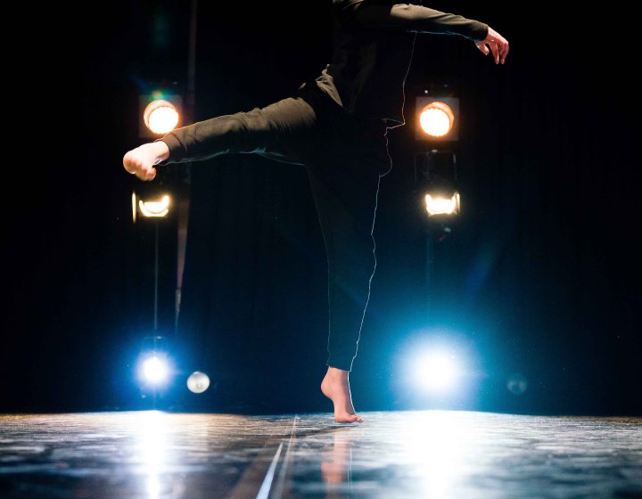 A young person making a dance pose towards the camera with stage lights shining in the background