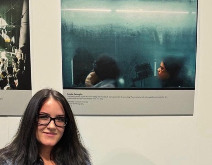 Photography student Natalie Persoglio standing next to her award-winning image of two people on a bus