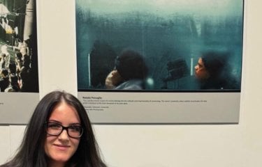 Photography student Natalie Persoglio standing next to her award-winning image of two people on a bus