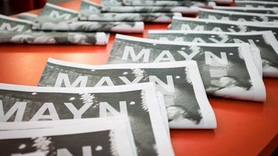 a row of newspapers with MAYN written on the front page