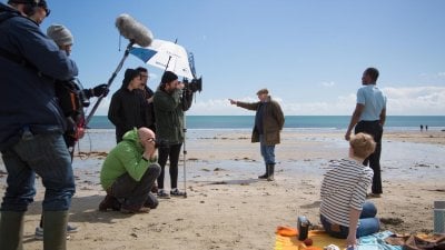 Film and TV students from Falmouth University filming a scene on a beach with blue sky