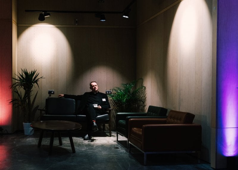 A man sat on a sofa in a darkly lit room with potted plants
