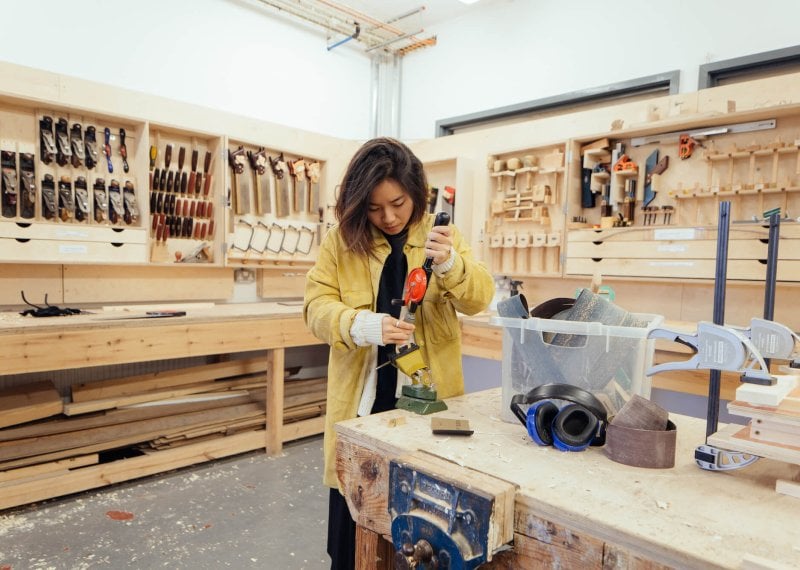Girl in yellow jacket working in wood workshop at Falmouth University