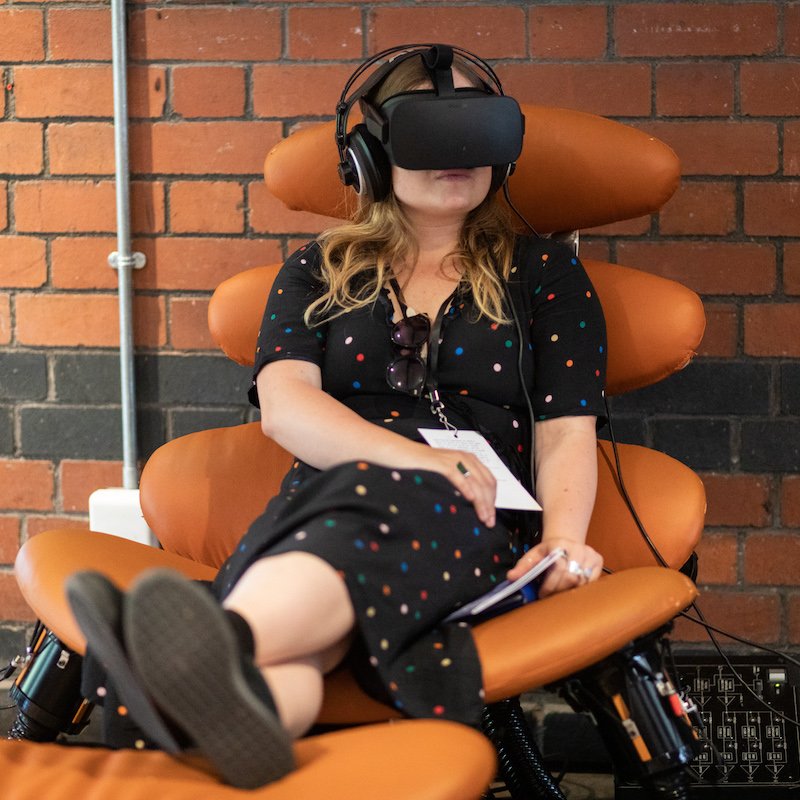 A woman sitting in an orange chair with VR headset on
