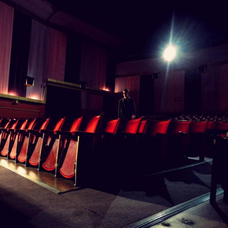 A man stood amongst red cinema seats, glare of the projector behind him.