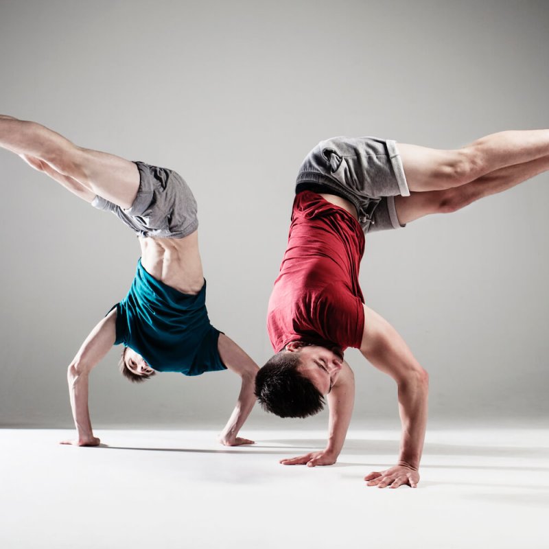 Two dancers doing hand stands and bending at hips so legs are at a right angle mirroring each other.