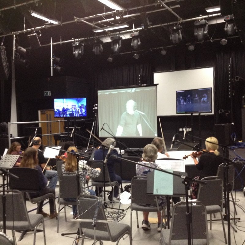 Group of musicians playing strings in front of a large screen