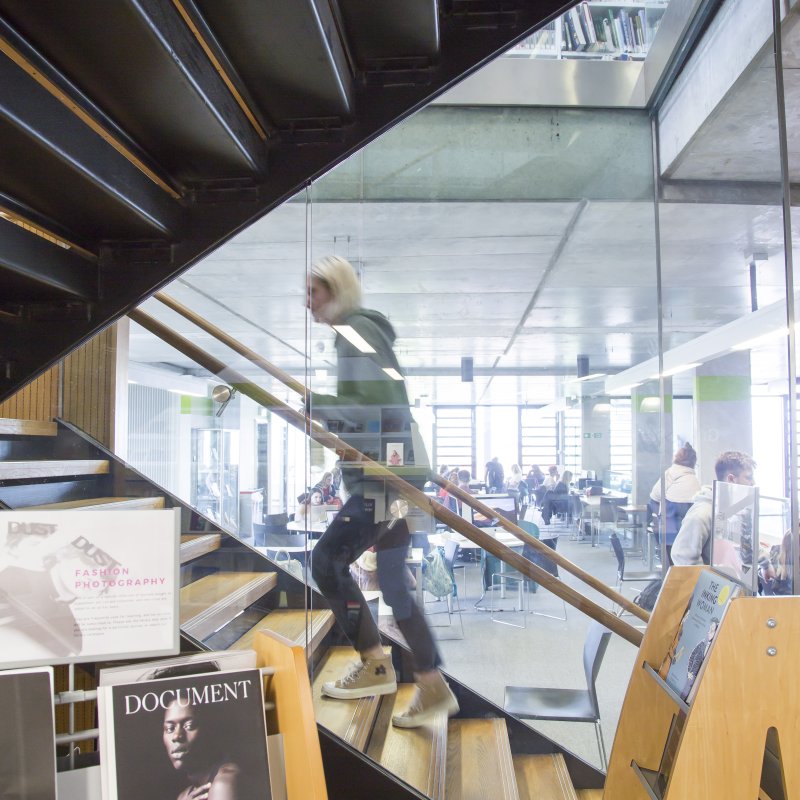 Female student walking up a staircase behind glass