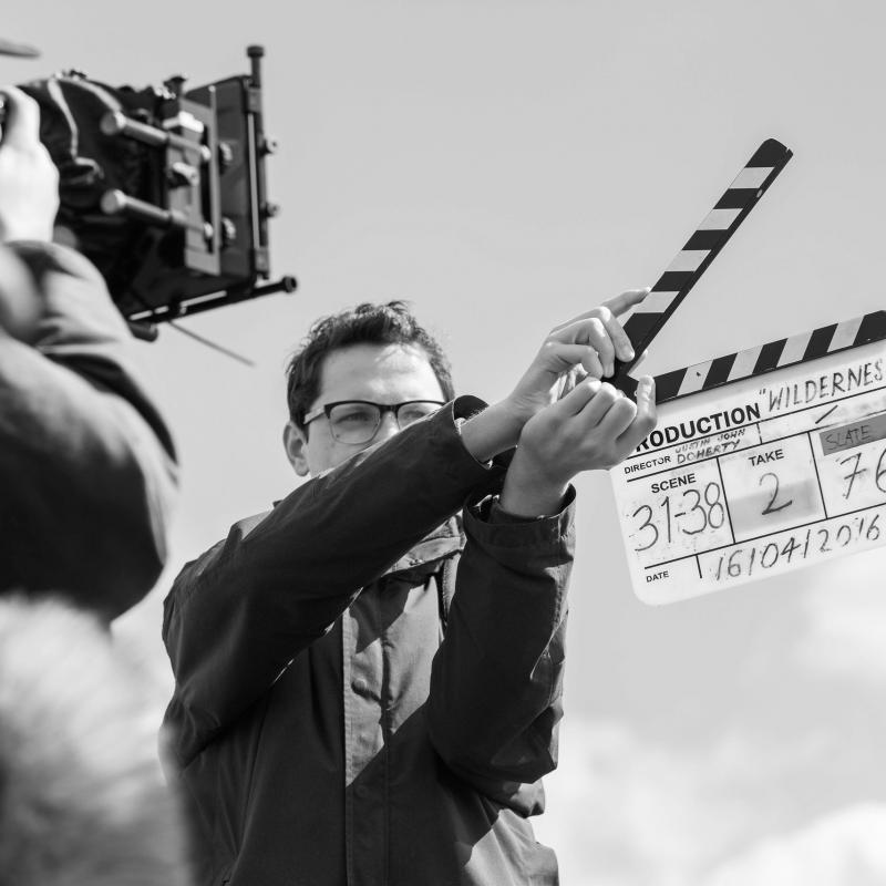 Grayscale image of Falmouth University student with clapperboard in front of camera.