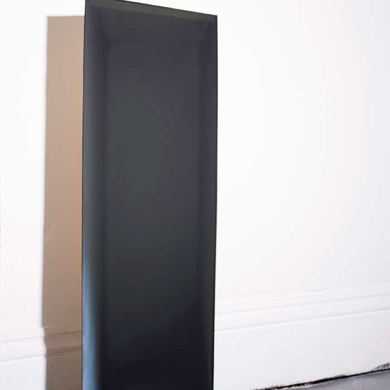A black rectangular sculpture propped up against a white wall