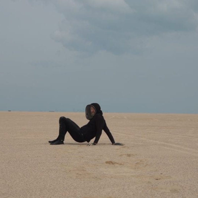 A man sat on a sandy surface in a desert