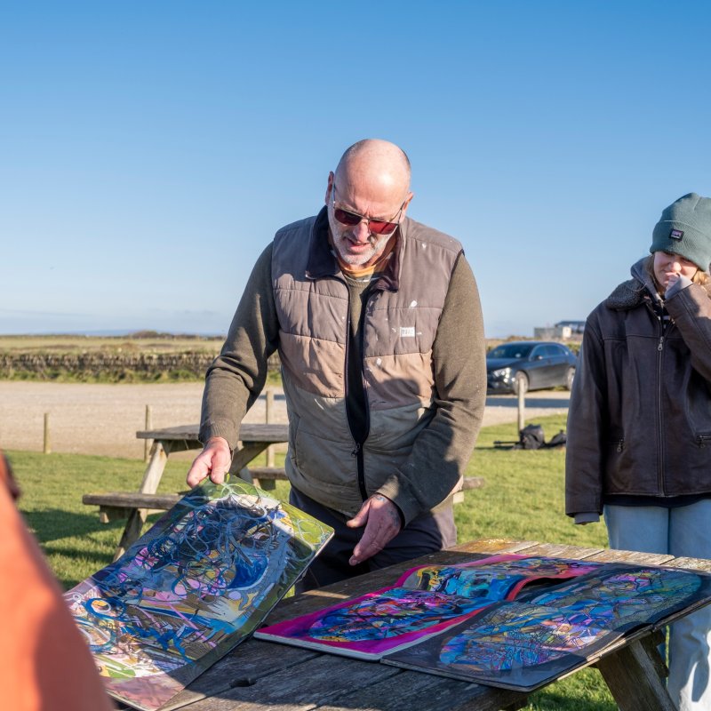 Artist Tony Plant shows plans to Falmouth University students during sand art project on Cornish beach 