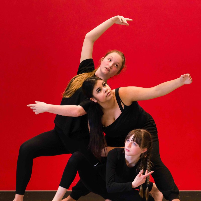 Three dancers pose against red background