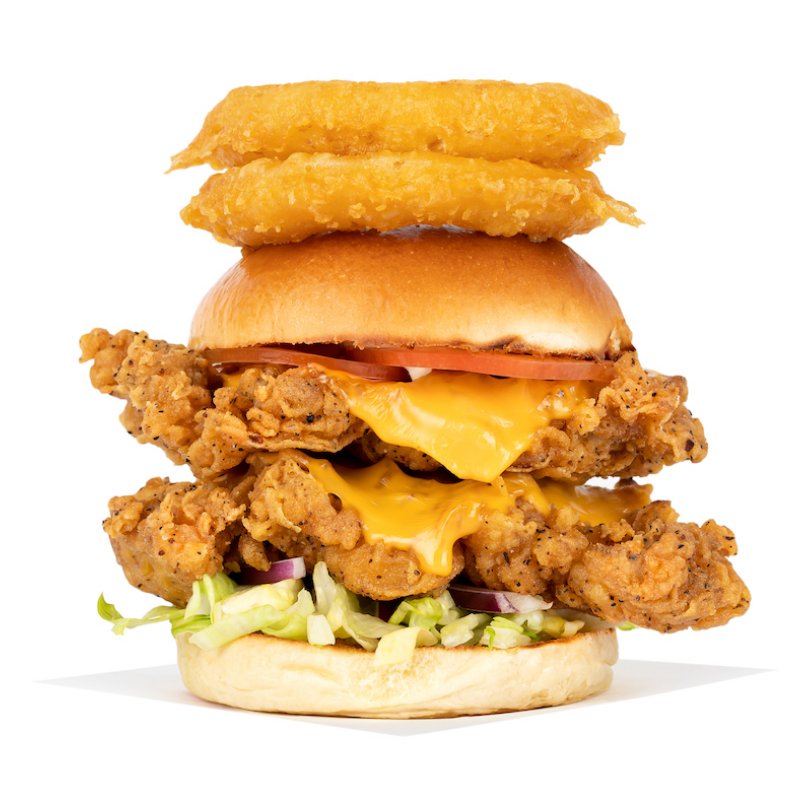 Two battered chicken fillets in a burger with onion rings on top 