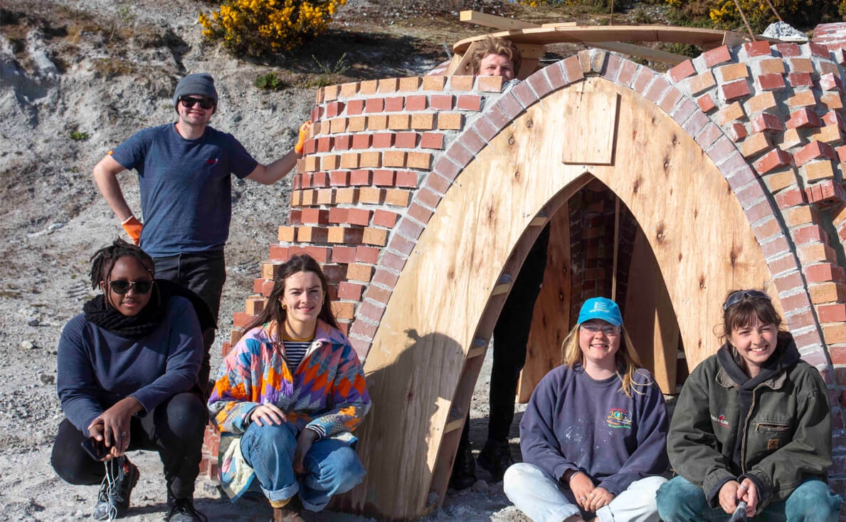 Architecture students outside a brick building with wooden arch