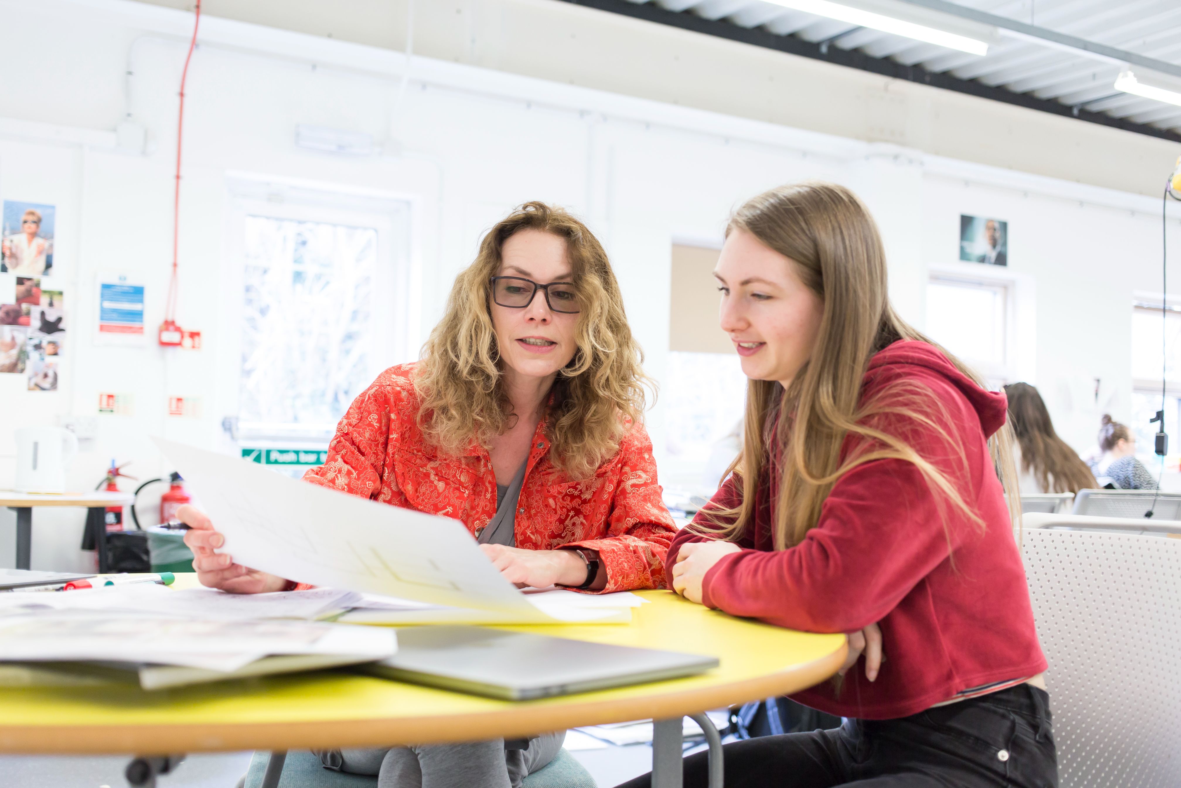 A woman sits next to a student, holding a piece of paper