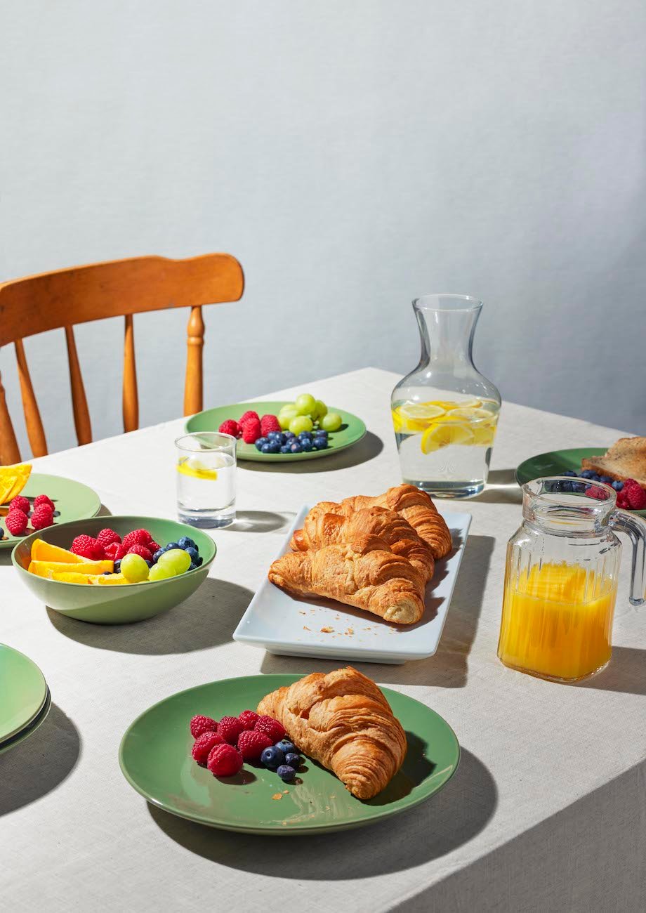 A table laid with croissants, fruit, orange juice and water