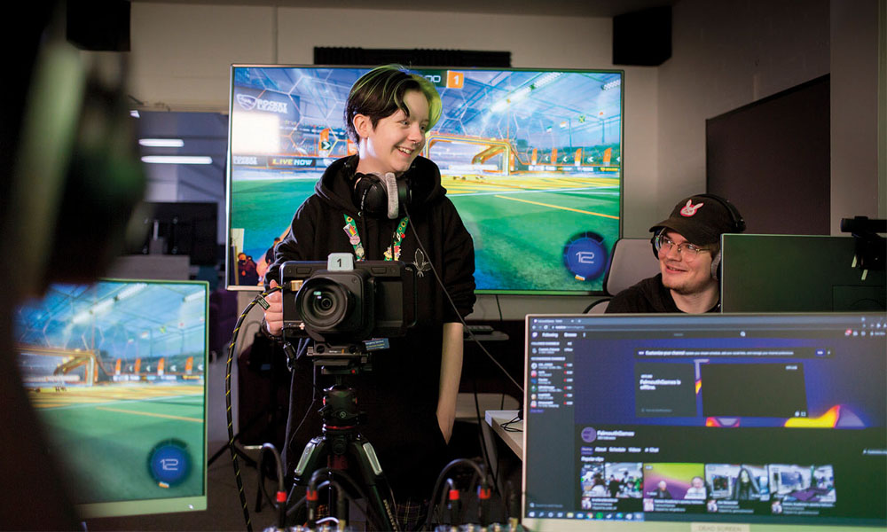 Esports students stood in front of digital screens with cameras