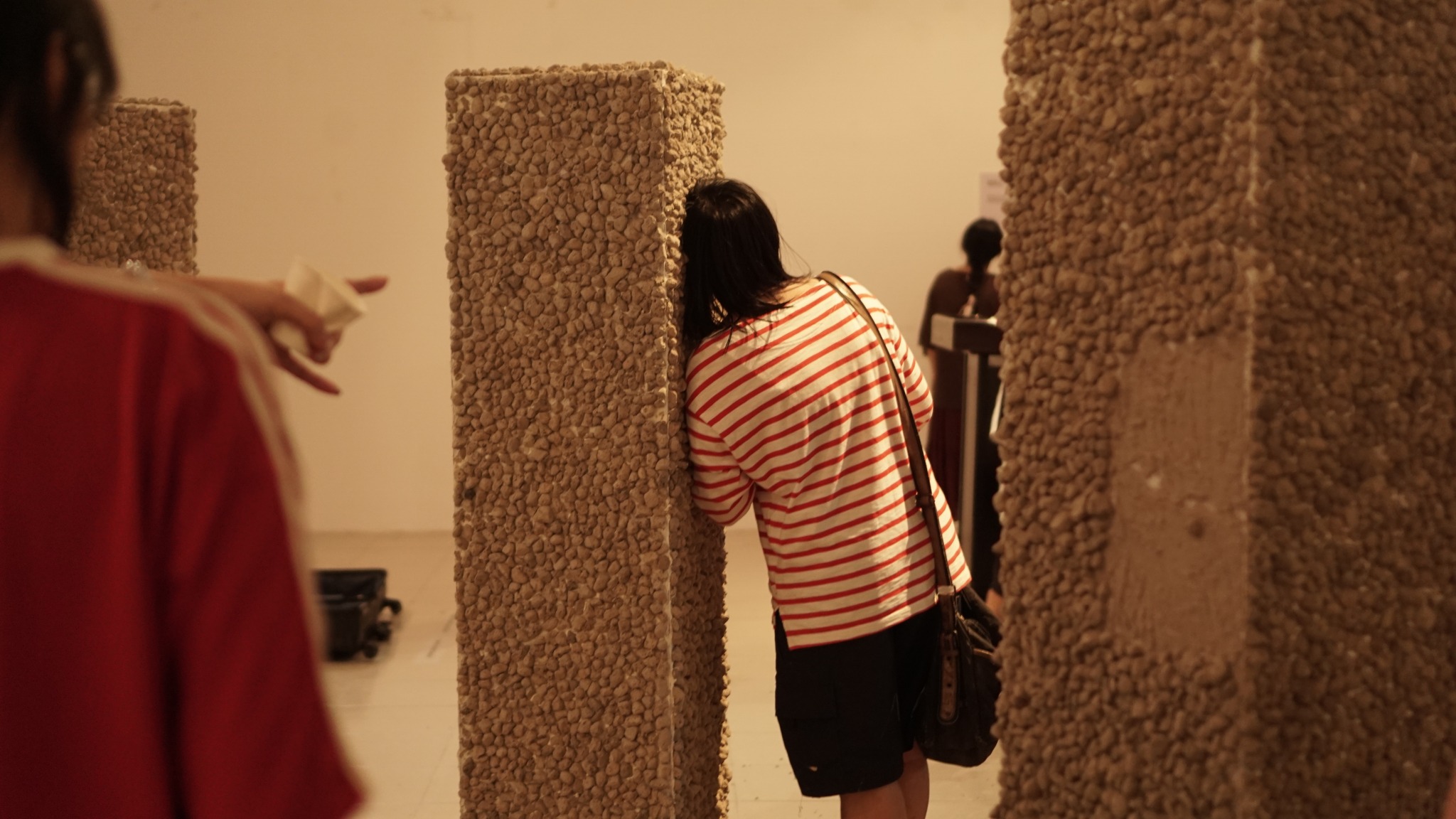 A student leans against a pillar-like sculpture covered in beige bobbled fabric, Falmouth University, Cornwall