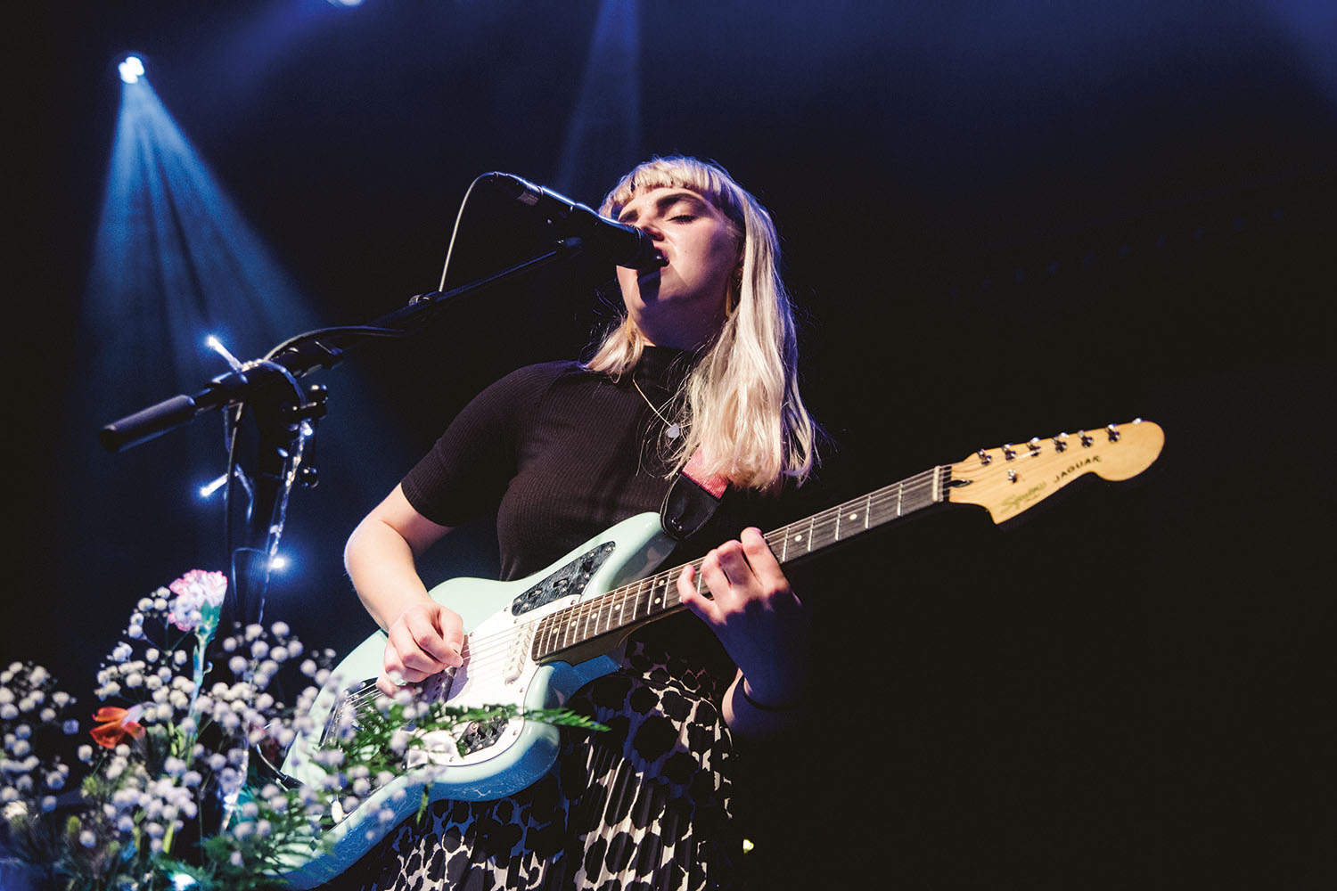 Student singing into microphone on stage and playing guitar