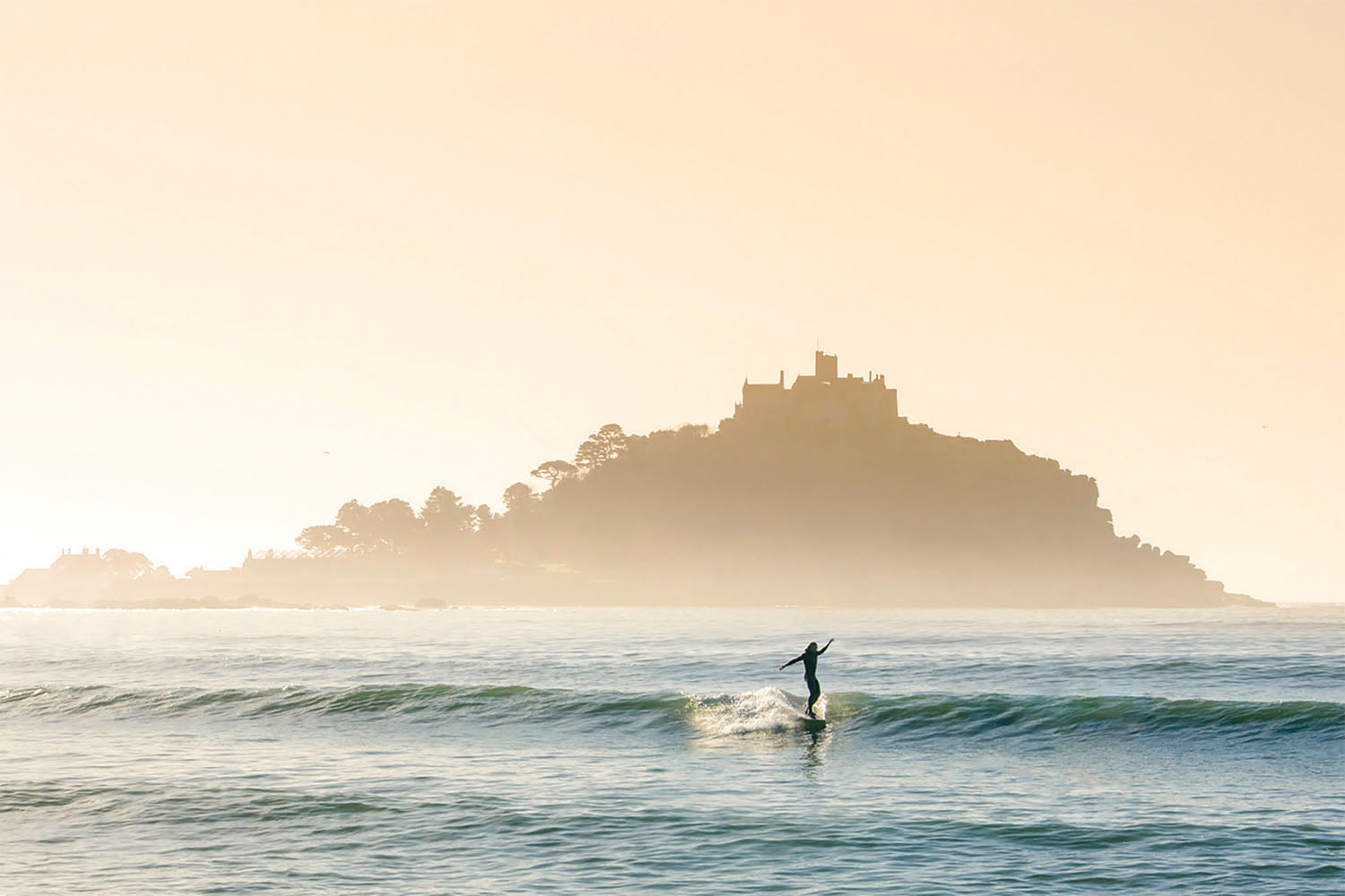 Surfer riding wave in front of St Michaels Mount