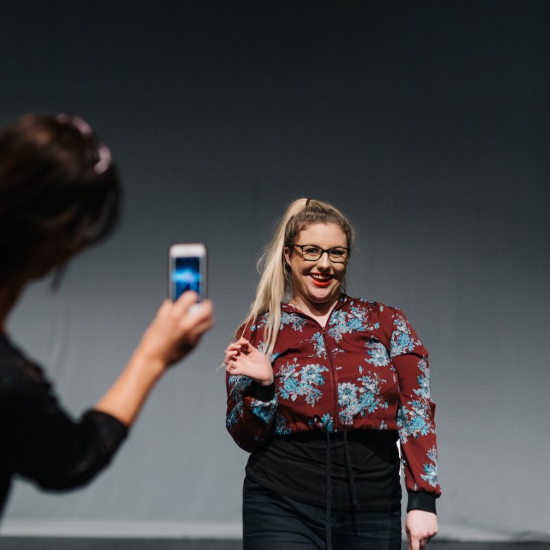 A student smiling while being filmed on a phone by another student