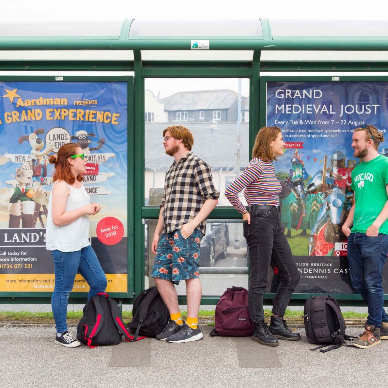 Students stood at bus stop leaning and chatting.