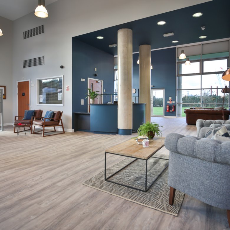 Modern open plan living area with grey armchair, wood flooring and large columns