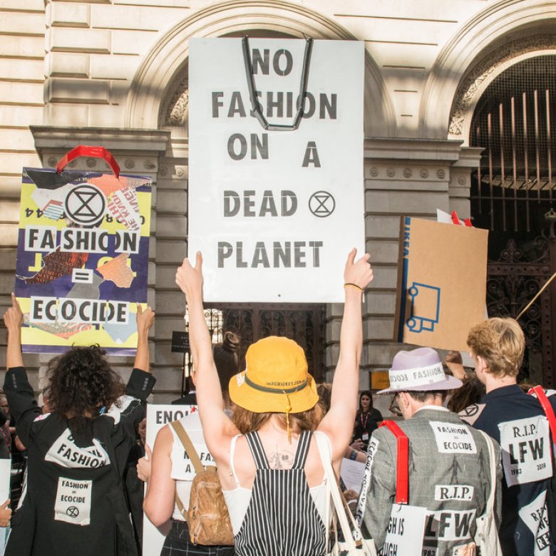 People gather to protest the fashion industry. A placard reads 'no fashion on a dead planet'
