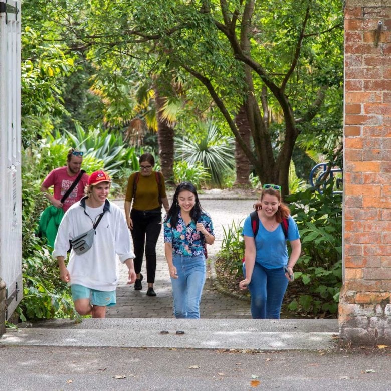 Students walking towards a gateway between red brick walls on Falmouth campus.