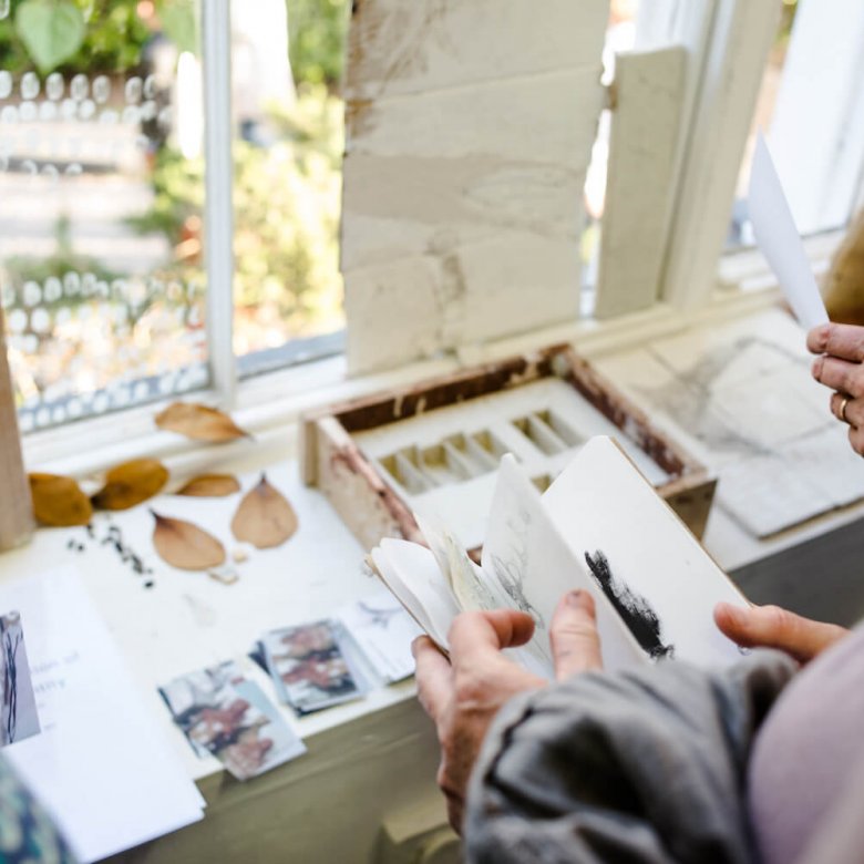 A close up of hands looking through sketchbooks and artworks on a table