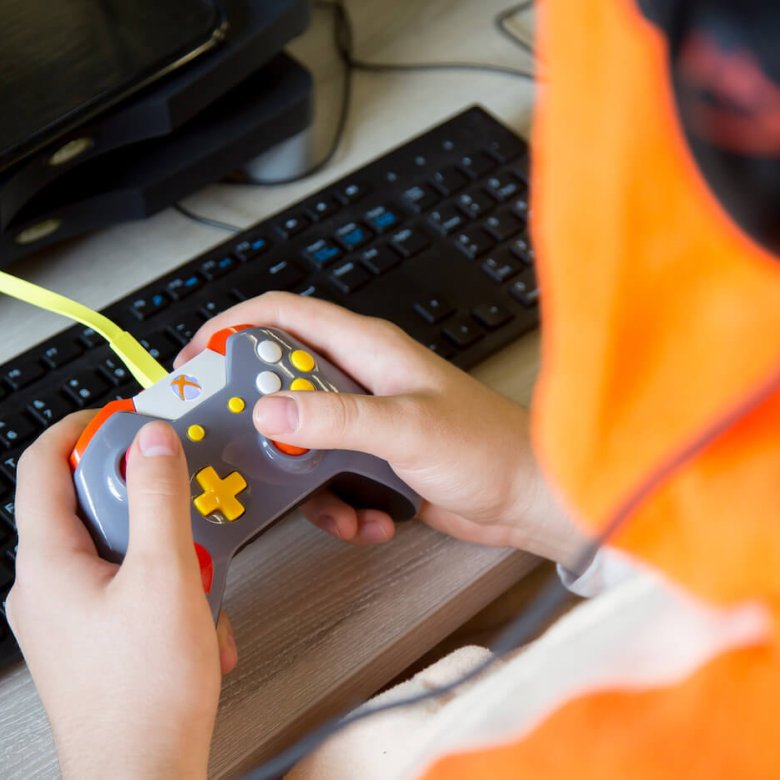 Hands holding a gaming controller in front of a computer keyboard