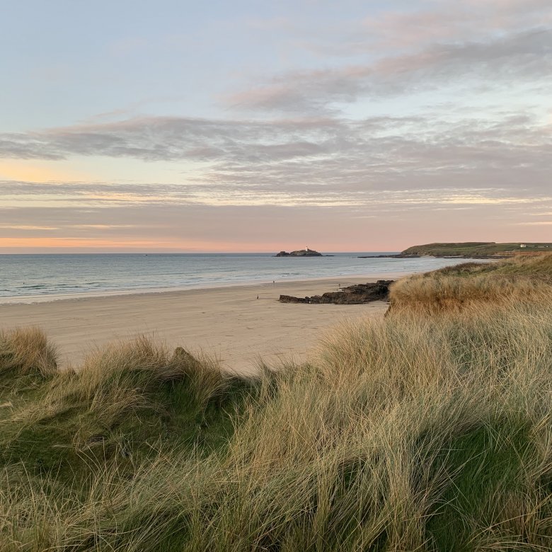 Godrevy beach with grass in the foreground and the sun setting in the background