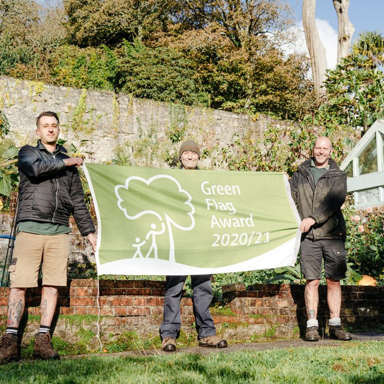 Three people holding up a banner in gardens