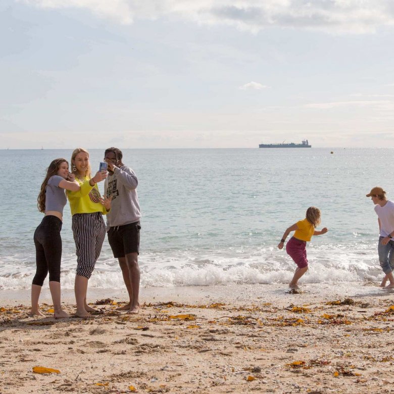 Five Falmouth University students on a sandy beach with the sea in the background