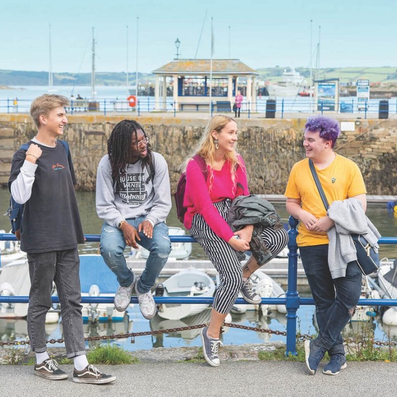 Falmouth University students sitting by the harbour on a sunny day