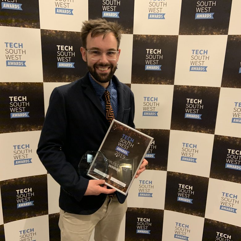 Lecturer holding the Tech South West Award, with a backdrop with branding on it.