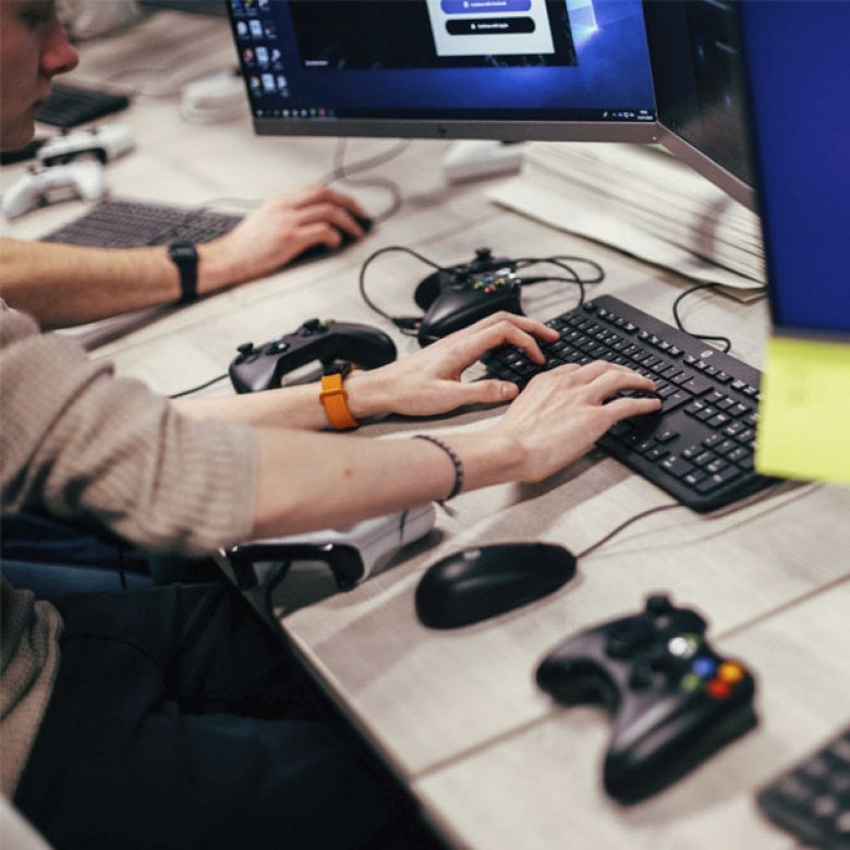 Hands typing on a keyboard with playstation controllers on the table