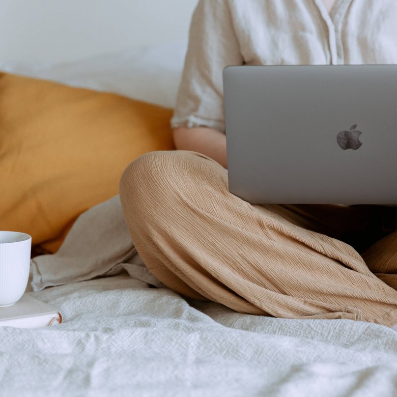 A person sat crossed legs with an apple mac and a cup