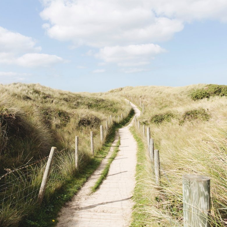 A narrow path through sand dunes with blue sky