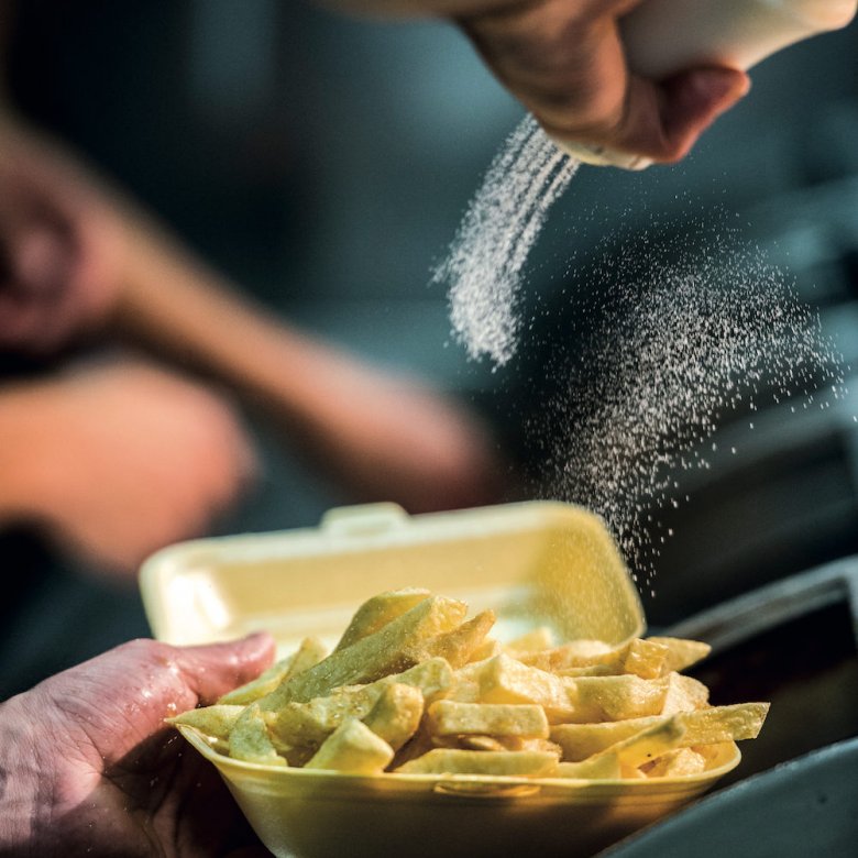 A hand pouring salt on a portion of chips