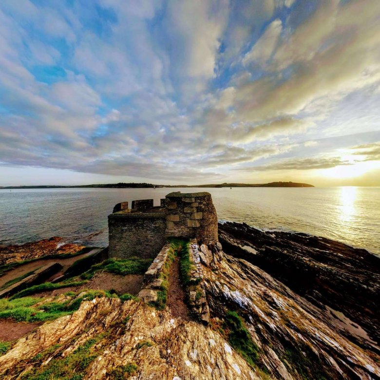 Ruins of a castle on a cliff with the sea and sun in the background