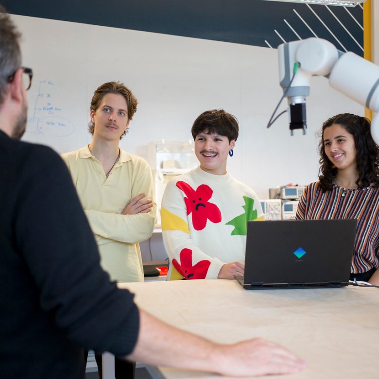 Falmouth University students listening to a lecturer around a table