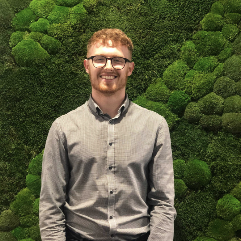 Will Dorrell Business and Entrepreneurship graduate standing in front of green moss wall.
