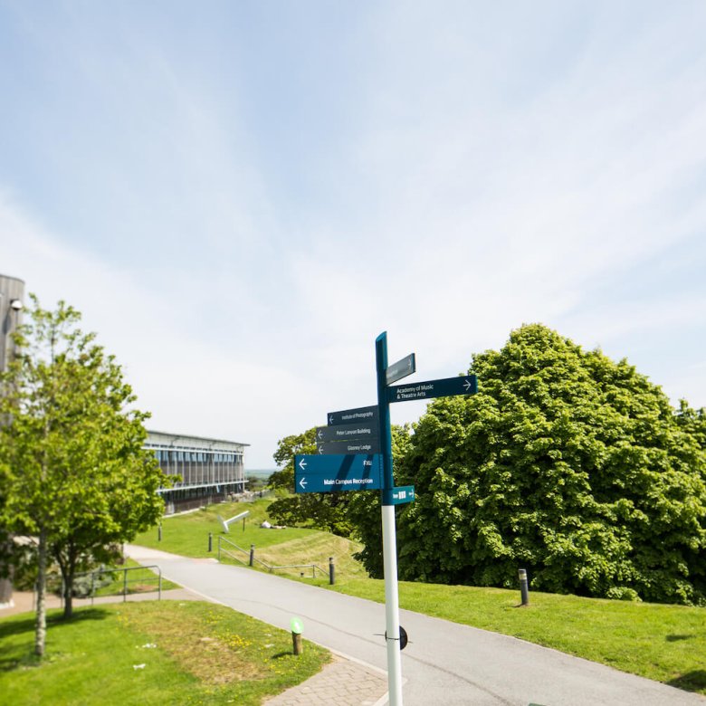 Blue signpost on Penryn Campus with trees and path